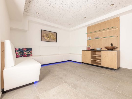 Ein feines Wellnesshotel in Fulpmes Moderner Wartebereich mit weißem Ecksofa und Holzschrank mit Glasregalen