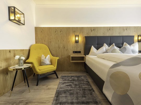 My hotel in Fulpmes in Stubaital Modern bedroom with yellow armchair, small table, and gray rug