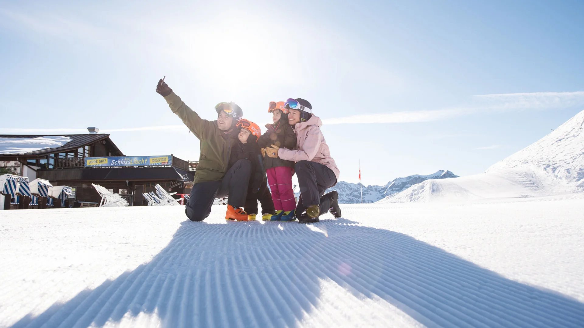 Four skiers pose in the snow against a snowy mountain landscape