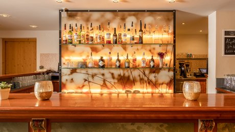 Einblicke in unser Hotel im Stubaital in Fulpmes Bar mit Holztheke und beleuchteter Rückwand mit Spirituosenflaschen