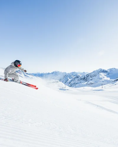 Der Alphof | Ihr Hotel in Fulpmes Skifahrer springt über eine verschneite Piste vor schneebedeckten Bergen