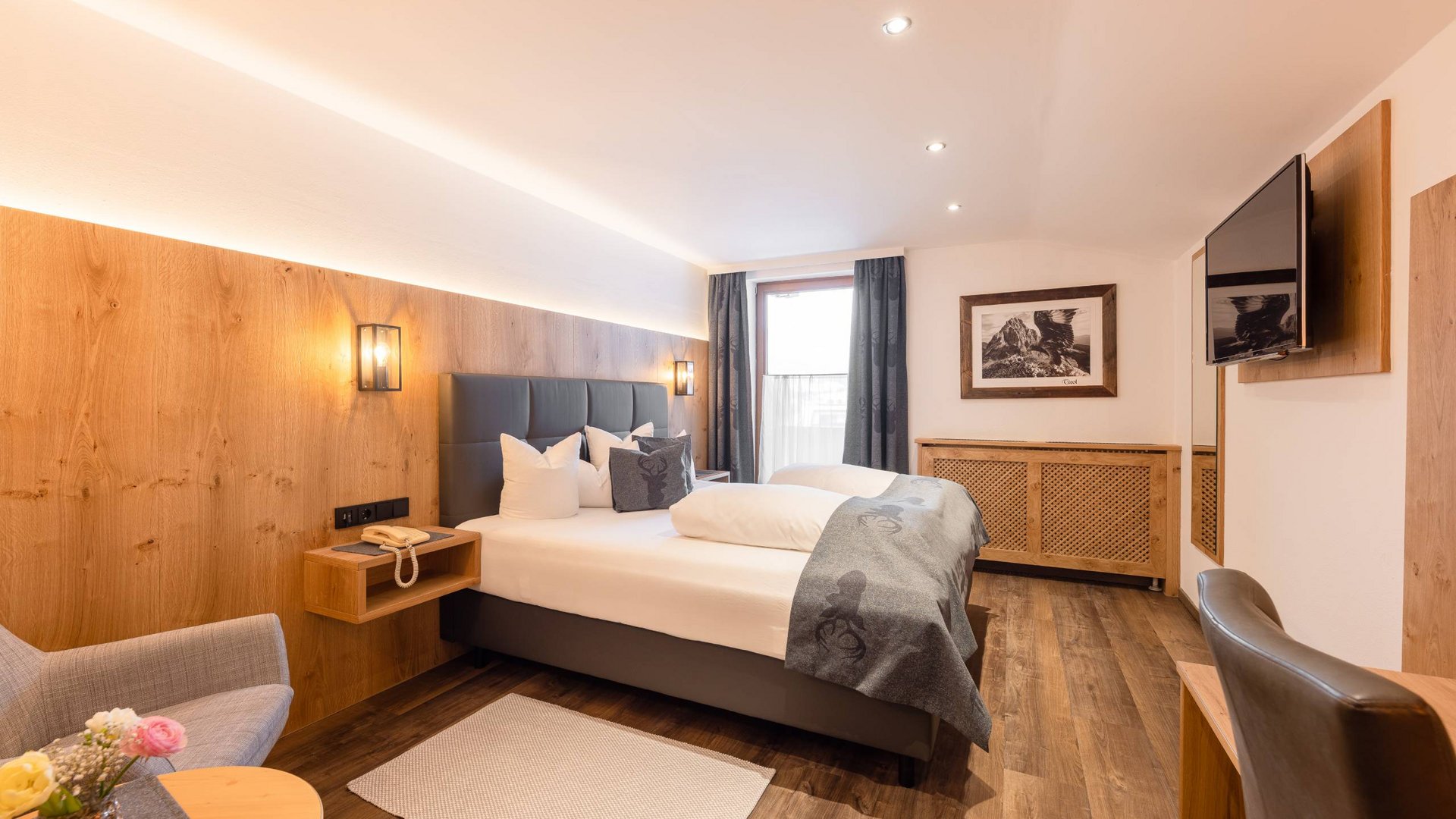 4-Sterne-Hotel Stubaital: Ihr Alphof erwartet Sie! Modernes Hotelzimmer mit Doppelbett, Sitzbereich und Fernseher an der Wand