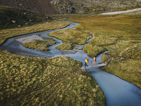 Sommerurlaub im Stubaital: nicht ohne meine Stubai Super Card Zwei Wanderer überqueren eine kleine Holzbrücke über einen gewundenen Bergbach