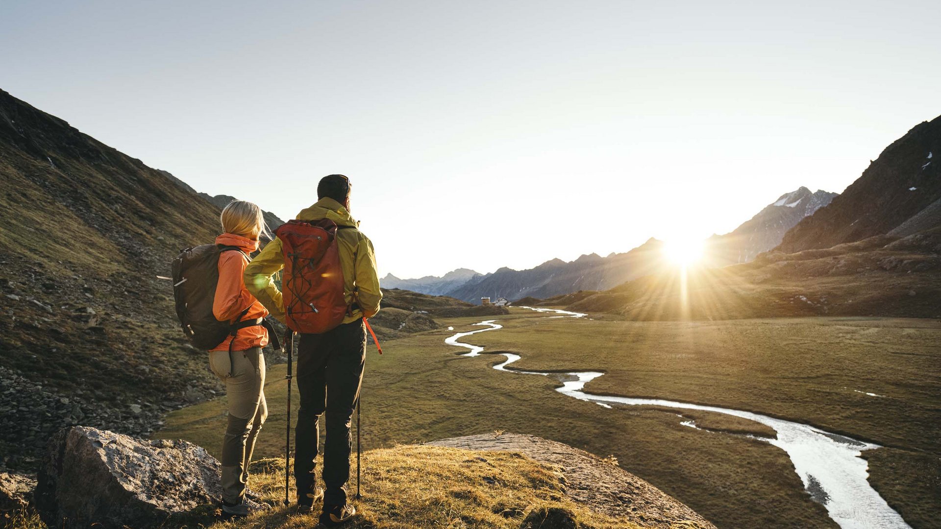 Sommerurlaub im Stubaital: nicht ohne meine Stubai Super Card Zwei Wanderer blicken bei Sonnenaufgang auf ein Tal mit einem gewundenen Fluss