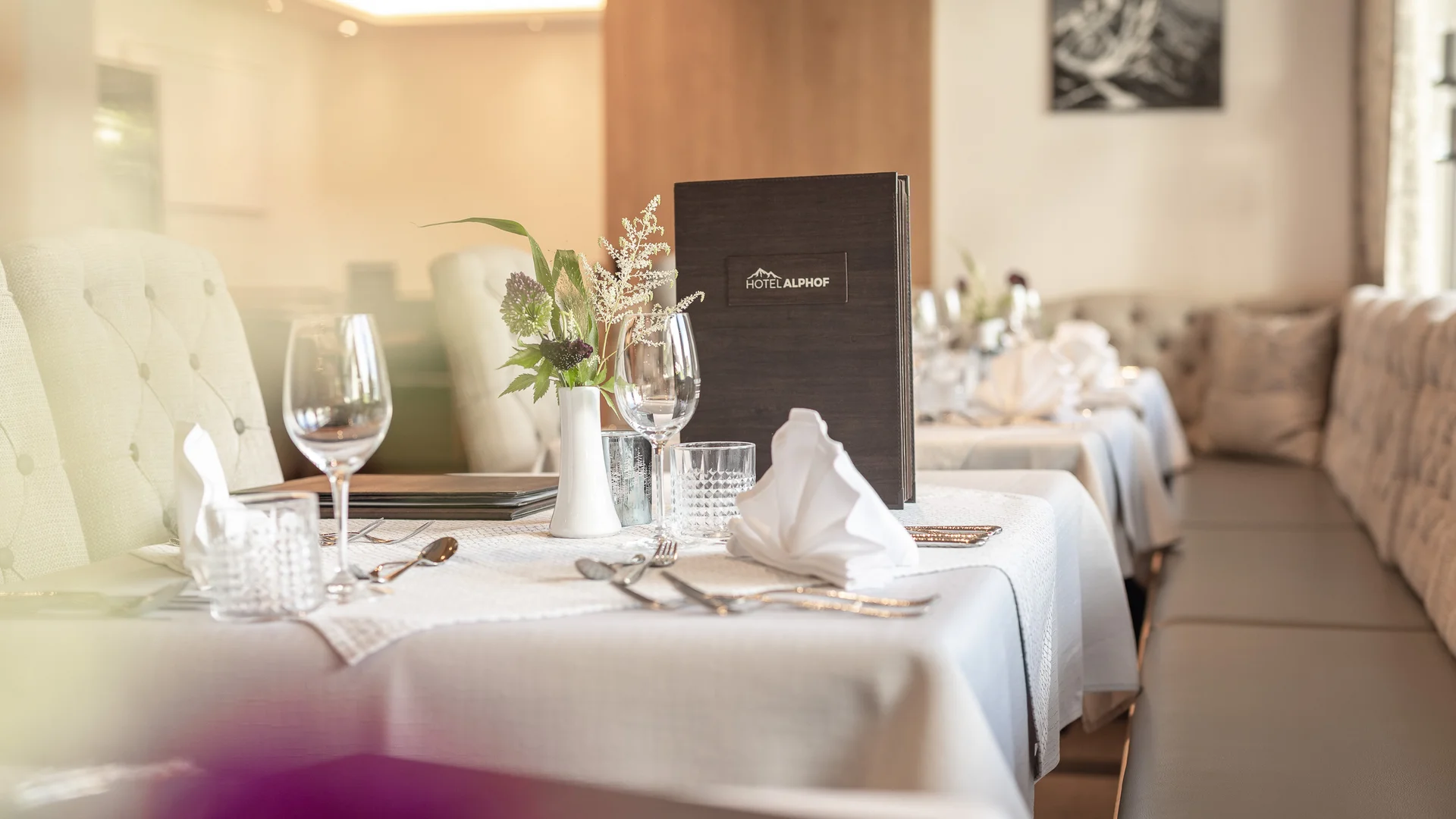 Elegant restaurant table with white tablecloth, wine glasses and flower arrangement