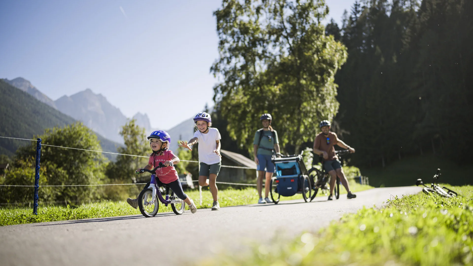 Family cycling with a child along a path against a mountain backdrop