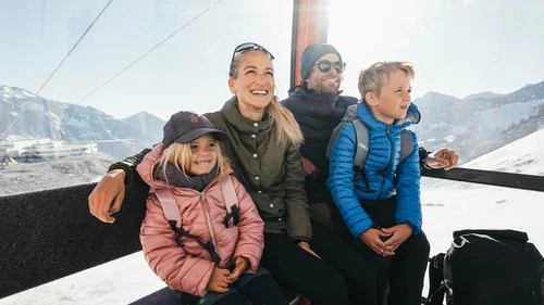 Family in a cable car with snow-covered mountains in the background