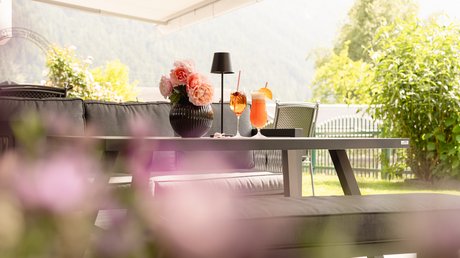 Einblicke in unser Hotel im Stubaital in Fulpmes Moderne Terrasse mit Sofa, Blumentopf und zwei Getränken auf dem Tisch bei Tageslicht