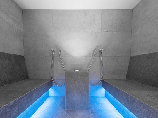 Unser Wellnesshotel im Stubaital Moderner Dampfbadraum mit grauen Fliesen und blauer Bodenbeleuchtung