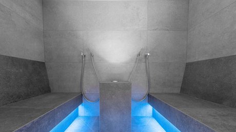 Einblicke in unser Hotel im Stubaital in Fulpmes Moderner Dampfbadraum mit grauen Fliesen und blauer Bodenbeleuchtung