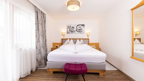Summer or winter holiday in Tyrol: Hotel Alphof in Fulpmes Bright bedroom with double bed, nightstands, gray curtains, and purple footstool