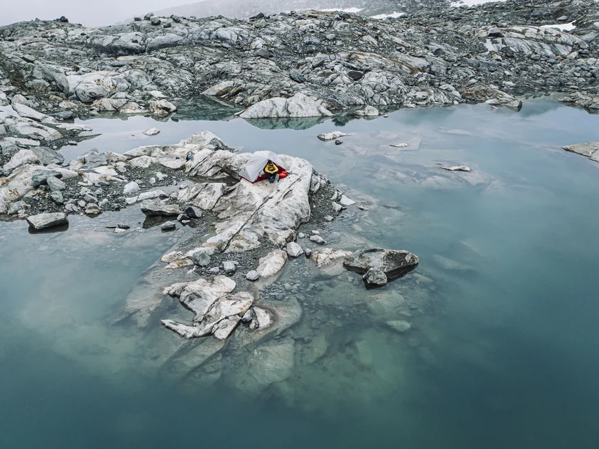Small tent on rocks beside a still mountain lake