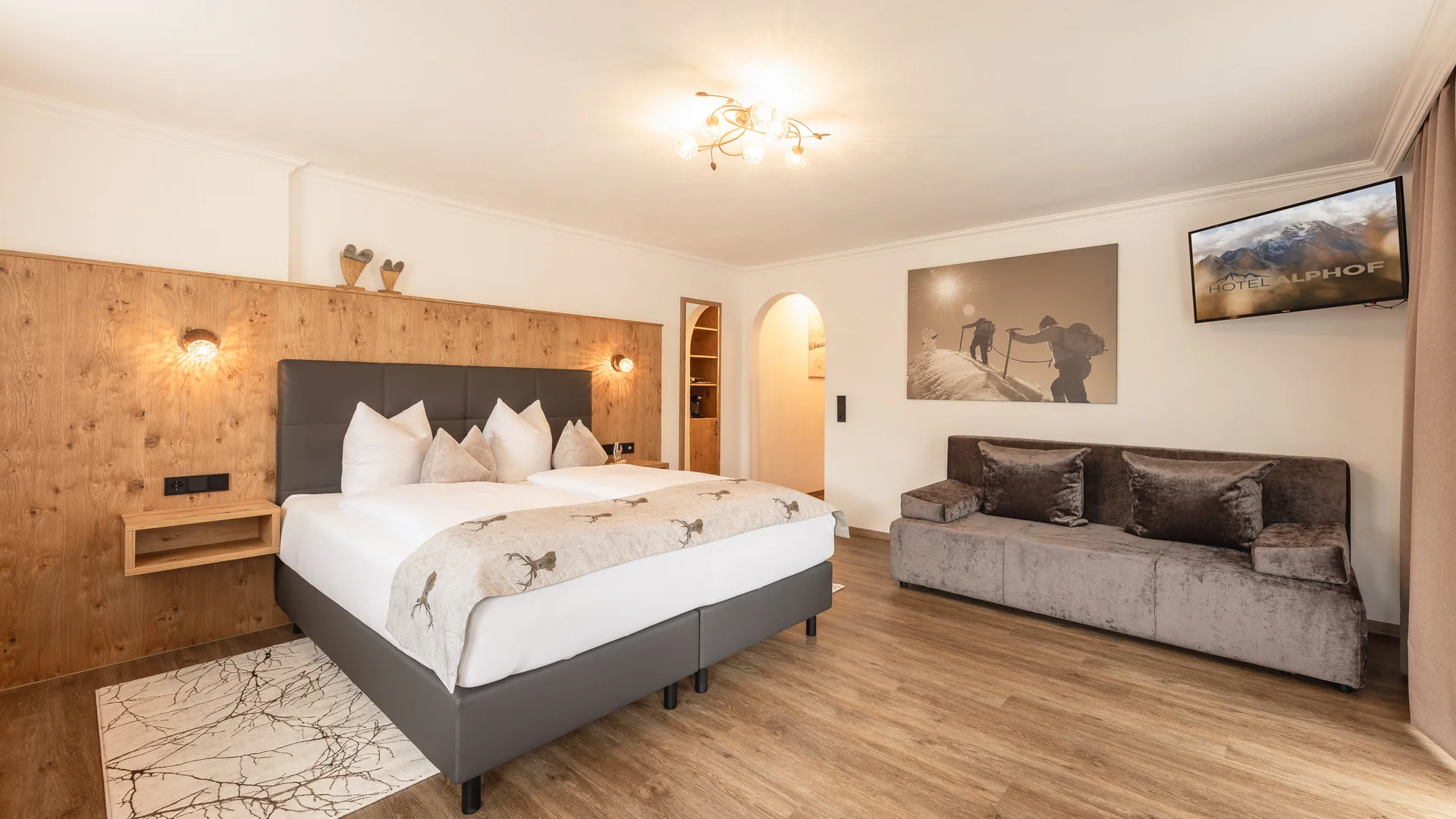 Bright hotel room with double bed, sofa, wood-paneled wall and TV