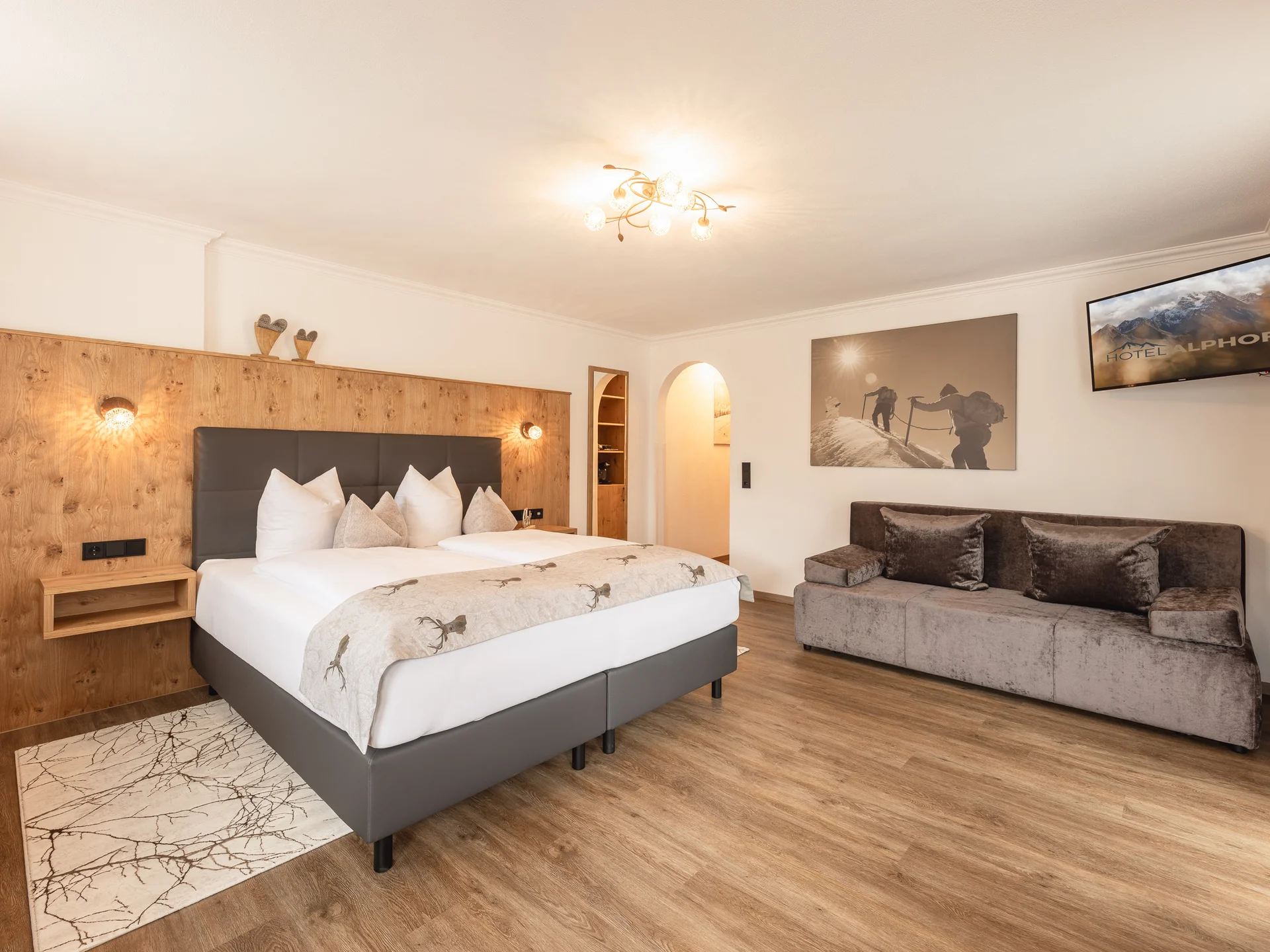 Der Alphof | Ihr Hotel in Fulpmes Helles Hotelzimmer mit Doppelbett, Sofa, Holzwand und Fernseher