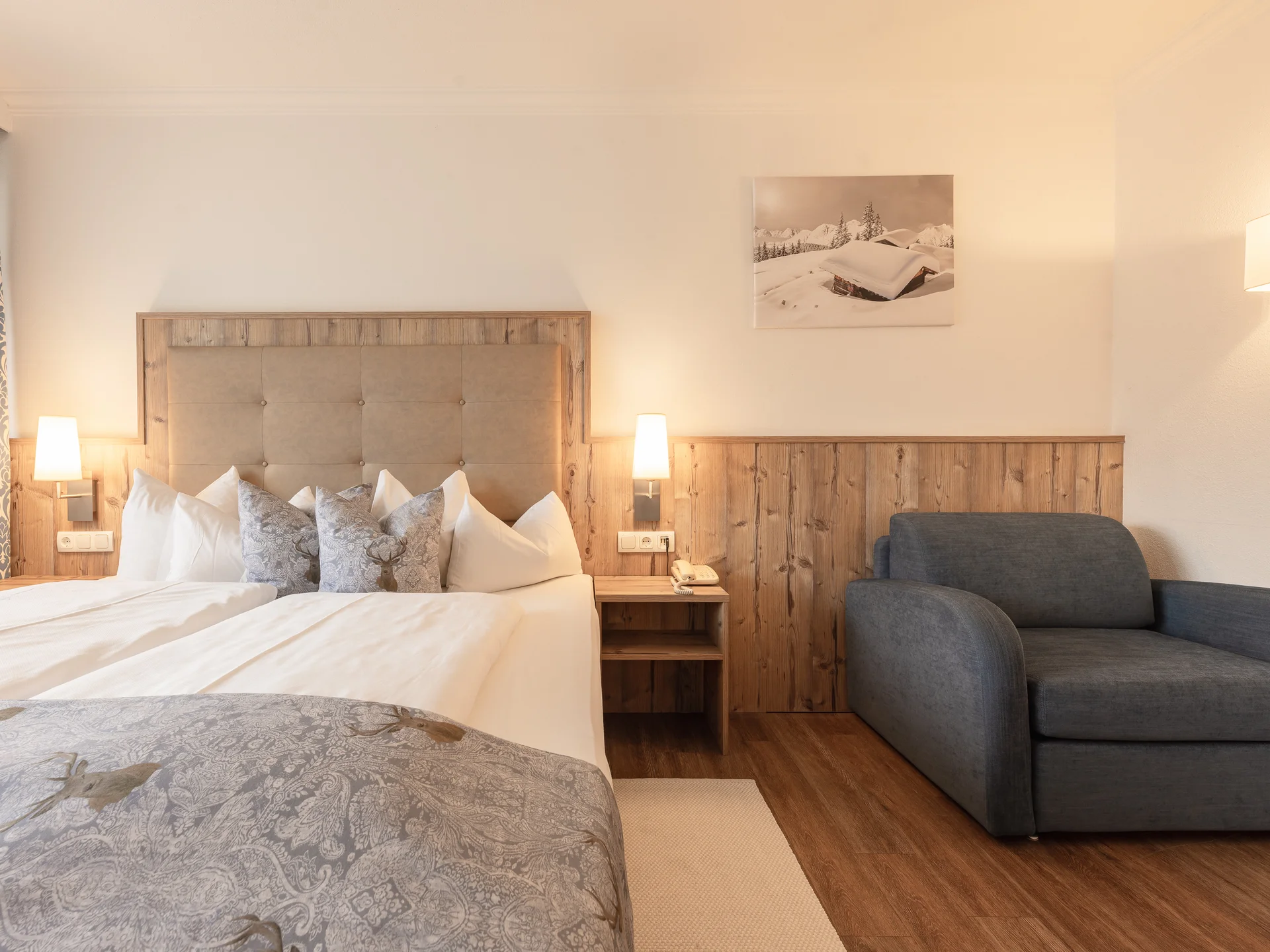 Der Alphof | Ihr Hotel in Fulpmes Hotelzimmer mit Doppelbett, Sessel, Holzwand und winterlichem Bild
