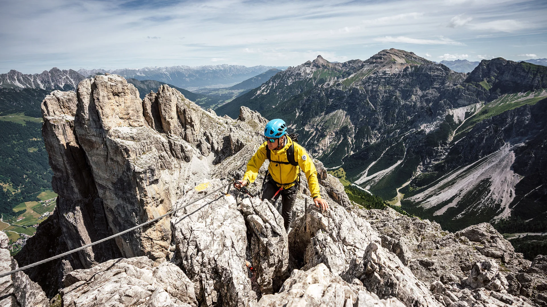 Mountaineer in a yellow jacket on a rocky ridge amid an alpine mountain landscape