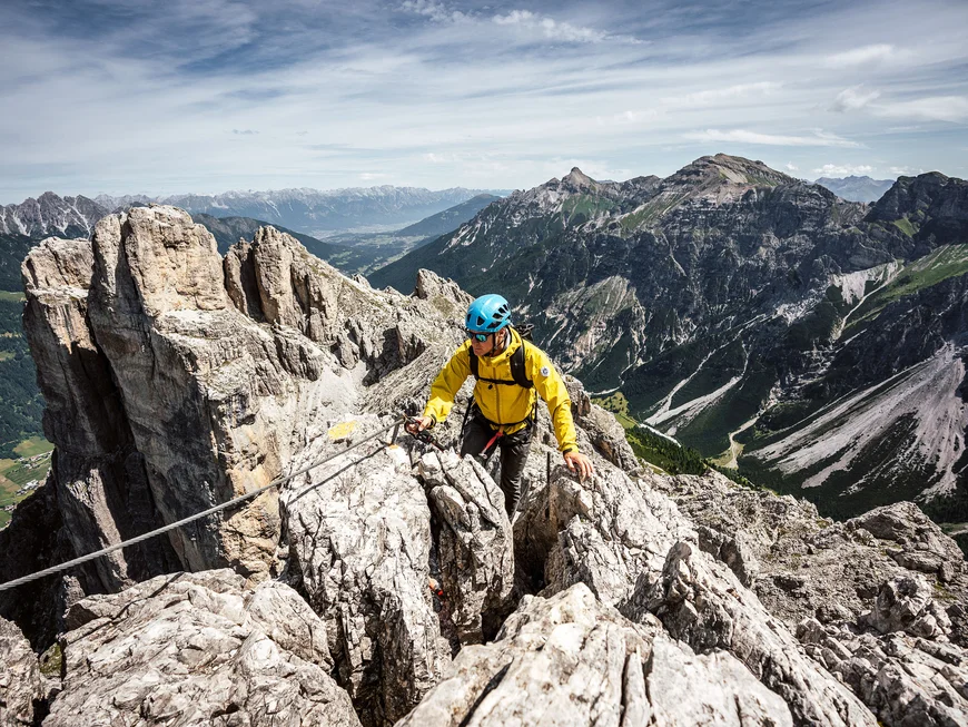 Mountaineer in a yellow jacket on a rocky ridge amid an alpine mountain landscape
