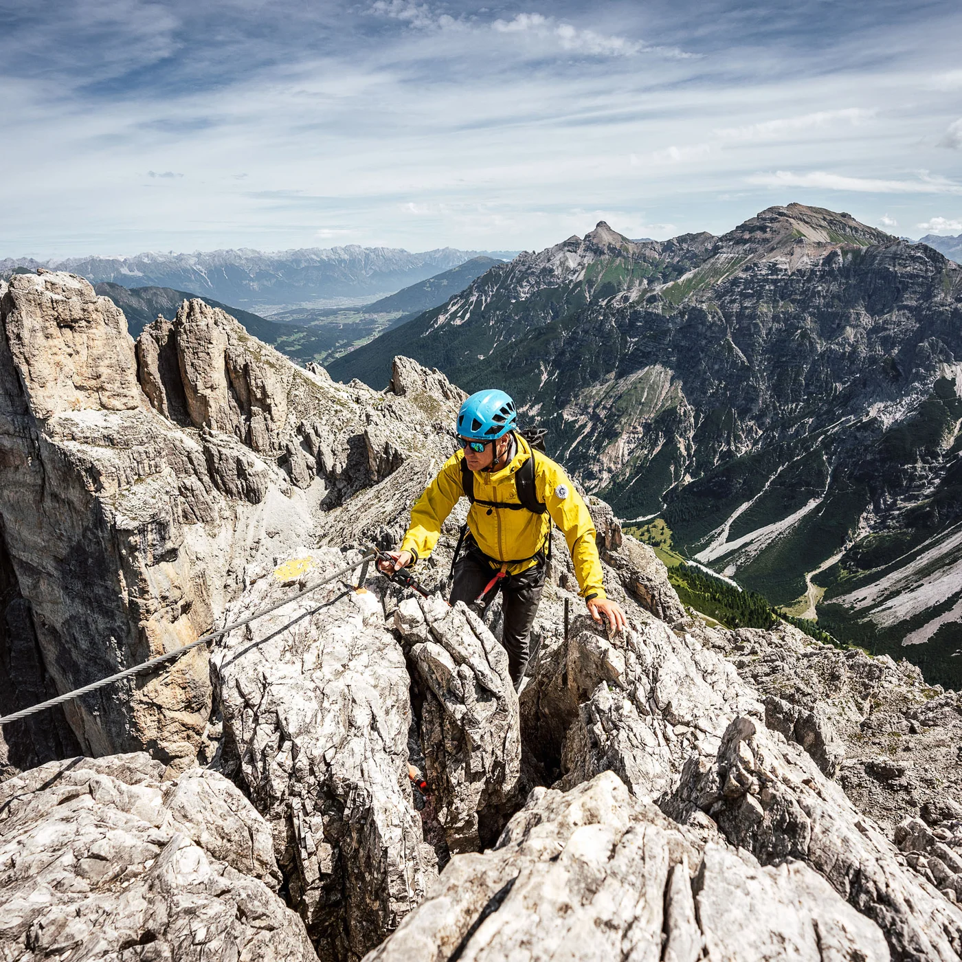 Mountaineer in a yellow jacket on a rocky ridge amid an alpine mountain landscape