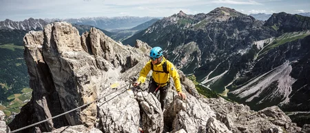 Mountaineer in a yellow jacket on a rocky ridge amid an alpine mountain landscape