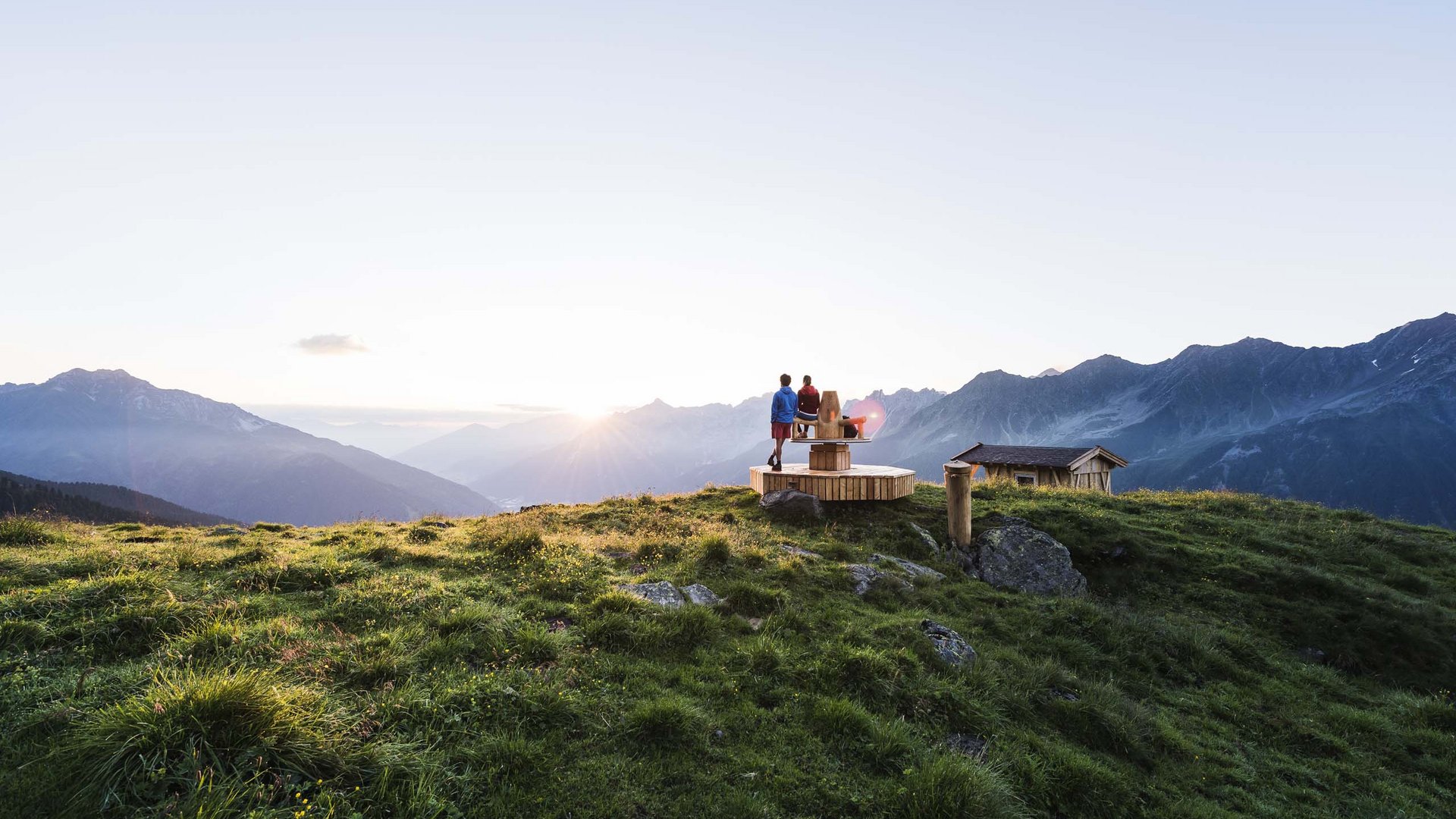 My Stubaital: a summer holiday at the Hotel Alphof Two people on wooden bench overlooking Alps at sunset